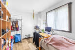 This cozy room features a functional desk area with a computer and ample storage solutions, including a large shelving unit and a clothing rack.