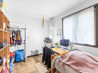 This cozy room features a functional desk area with a computer and ample storage solutions, including a large shelving unit and a clothing rack.