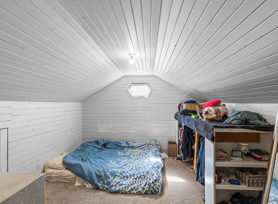 Discover this charming attic bedroom, featuring a cozy bed with blue patterned bedding and a unique hexagonal window that floods the space with natural light.