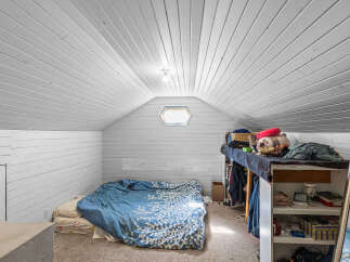 Discover this charming attic bedroom, featuring a cozy bed with blue patterned bedding and a unique hexagonal window that floods the space with natural light.