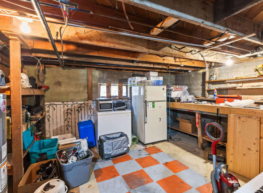 Discover ample storage and utility in this basement featuring a large workbench, a refrigerator, and a freezer, perfect for organizing your belongings.