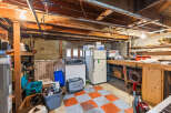 Discover ample storage and utility in this basement featuring a large workbench, a refrigerator, and a freezer, perfect for organizing your belongings.