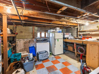 Discover ample storage and utility in this basement featuring a large workbench, a refrigerator, and a freezer, perfect for organizing your belongings.