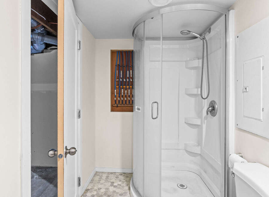 This bathroom features a modern, curved glass shower stall with multiple shelves and a handheld showerhead.