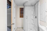 This bathroom features a modern, curved glass shower stall with multiple shelves and a handheld showerhead.