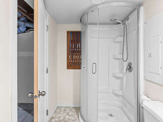 This bathroom features a modern, curved glass shower stall with multiple shelves and a handheld showerhead.