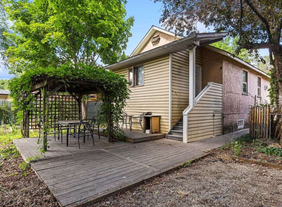 Enjoy outdoor living with this charming backyard featuring a wooden deck and a covered pergola adorned with lush greenery.