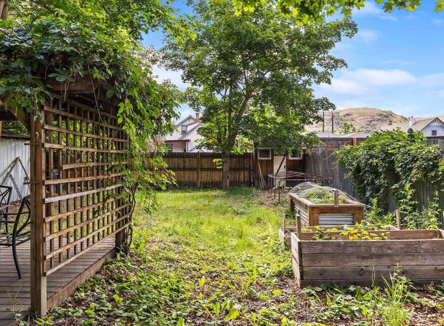 Discover your private oasis in this charming backyard, featuring a wooden pergola draped in lush greenery, perfect for outdoor relaxation.