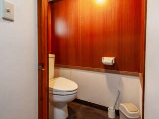 Step into this cozy bathroom featuring a clean white toilet and a convenient toilet paper holder mounted on the warm, wood-paneled wall.