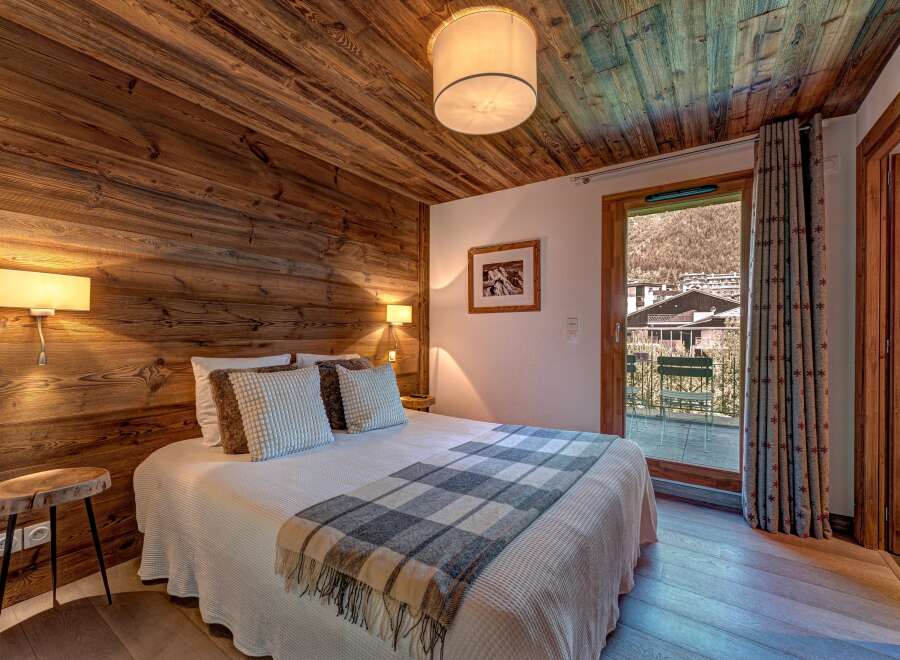 Experience rustic charm in this cozy bedroom, featuring warm wooden walls and ceiling, complemented by a plush bed adorned with a classic plaid throw.