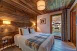 Experience rustic charm in this cozy bedroom, featuring warm wooden walls and ceiling, complemented by a plush bed adorned with a classic plaid throw.