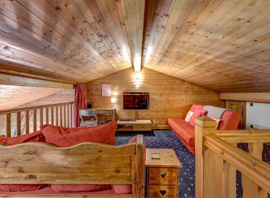 Experience cozy living in this charming wooden loft, featuring a comfortable red sofa and a rustic wooden bench with heart details.