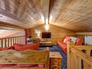 Experience cozy living in this charming wooden loft, featuring a comfortable red sofa and a rustic wooden bench with heart details.