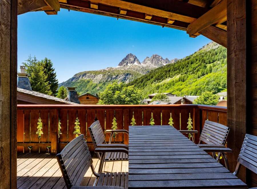 Enjoy breathtaking mountain views from this charming chalet's private balcony, complete with a rustic wooden table and chairs.