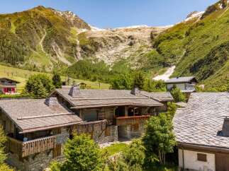 Experience alpine living in this stunning mountain chalet, featuring rustic stone and timber construction set against a breathtaking backdrop of snow-capped peaks and lush green slopes.