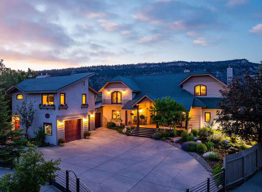 Experience luxury living in this stunning mountain home, featuring a grand entrance with a covered porch and inviting rocking chairs.