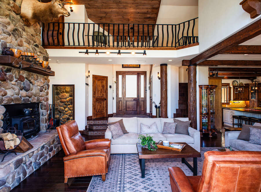 Experience rustic luxury in this stunning lodge-style living room, featuring a grand stone fireplace and exposed wooden beams.