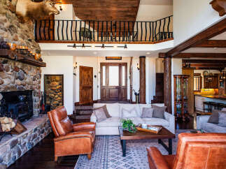 Experience rustic luxury in this stunning lodge-style living room, featuring a grand stone fireplace and exposed wooden beams.
