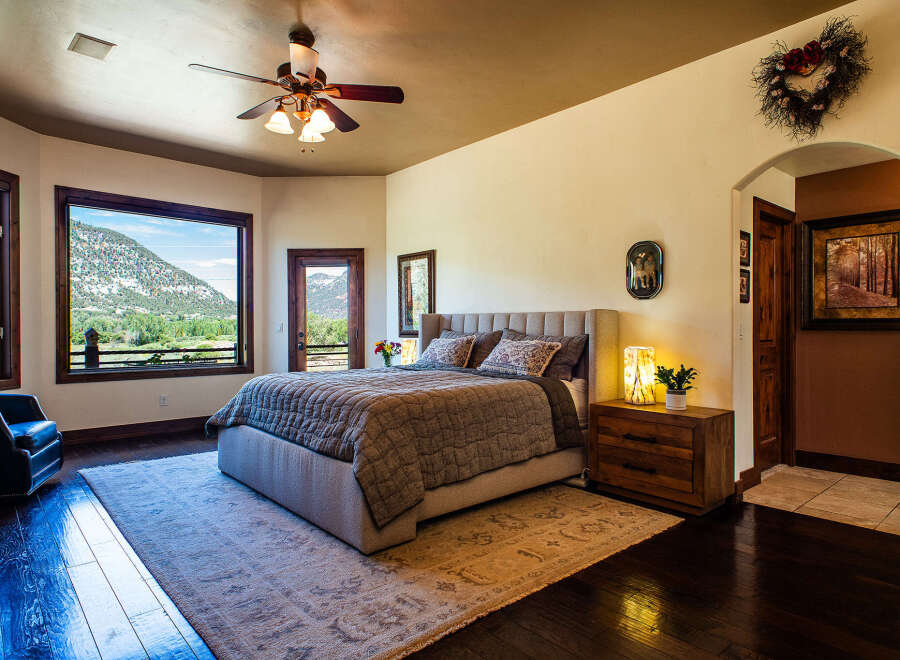 Experience breathtaking mountain views from this luxurious master bedroom, featuring a king-sized bed with a plush headboard and a cozy quilted comforter.