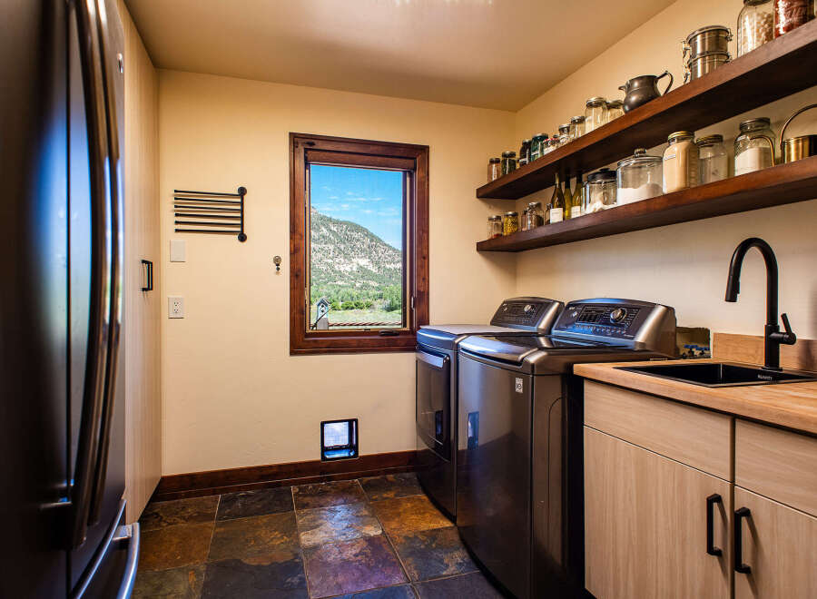 This laundry room boasts modern stainless steel appliances, including a washer and dryer, complemented by a sleek black sink and faucet.