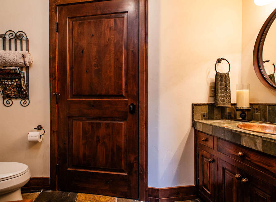 This bathroom features a rich, dark wood door and cabinetry, complemented by a copper sink and a slate tile countertop.