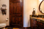This bathroom features a rich, dark wood door and cabinetry, complemented by a copper sink and a slate tile countertop.
