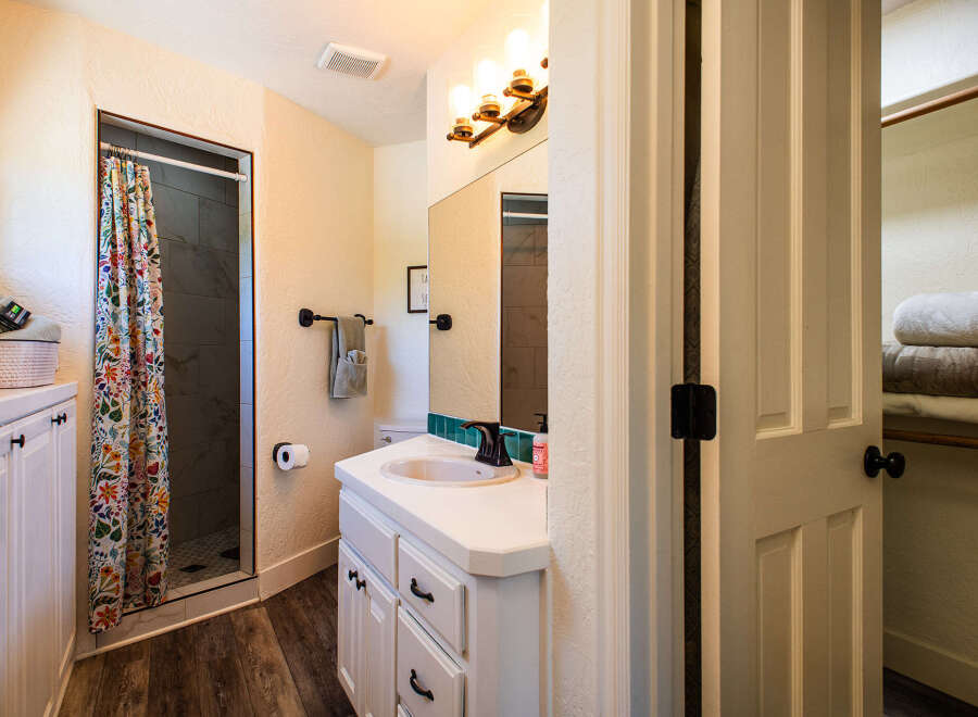 This charming bathroom features a vibrant floral shower curtain, a modern vanity with a vessel sink, and a spacious walk-in closet.