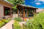 Discover this charming property featuring a rustic wooden greenhouse, perfect for gardening enthusiasts, alongside a cozy home with a distinctive red-trimmed window.