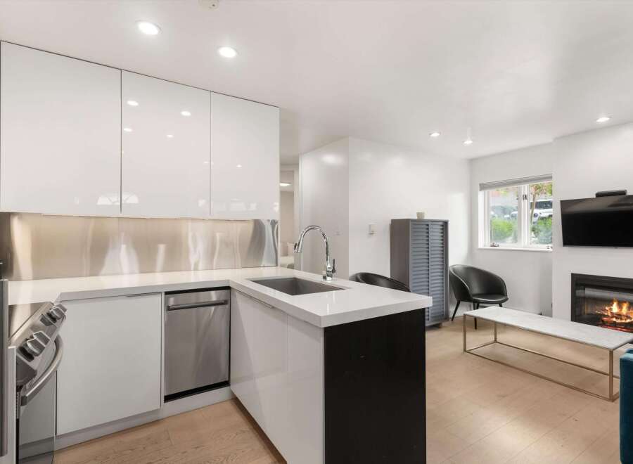 Experience modern living in this sleek kitchen featuring high-gloss white cabinetry and a stainless steel backsplash.