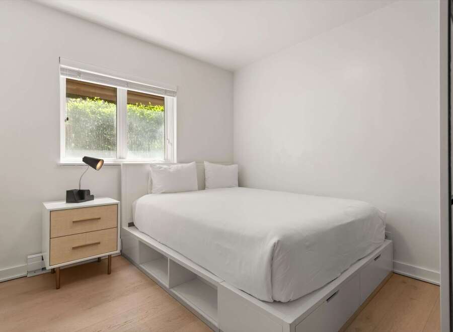 This minimalist bedroom features a comfortable queen-size bed with crisp white linens, complemented by a sleek nightstand with ample storage.