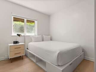 This minimalist bedroom features a comfortable queen-size bed with crisp white linens, complemented by a sleek nightstand with ample storage.