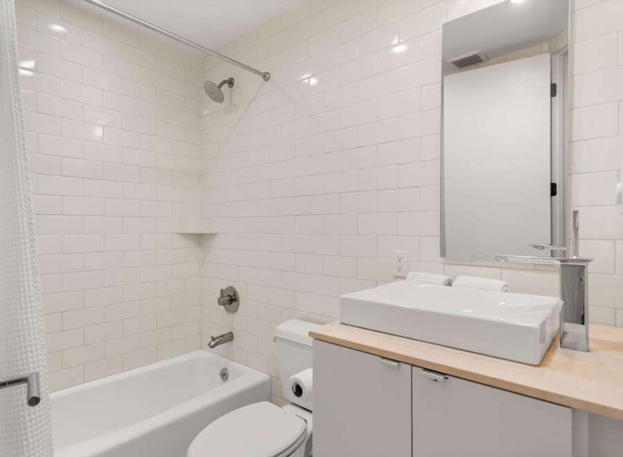 This modern bathroom features a pristine white subway tile shower and tub surround, complemented by a sleek vessel sink atop a light wood vanity.