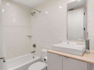 This modern bathroom features a pristine white subway tile shower and tub surround, complemented by a sleek vessel sink atop a light wood vanity.
