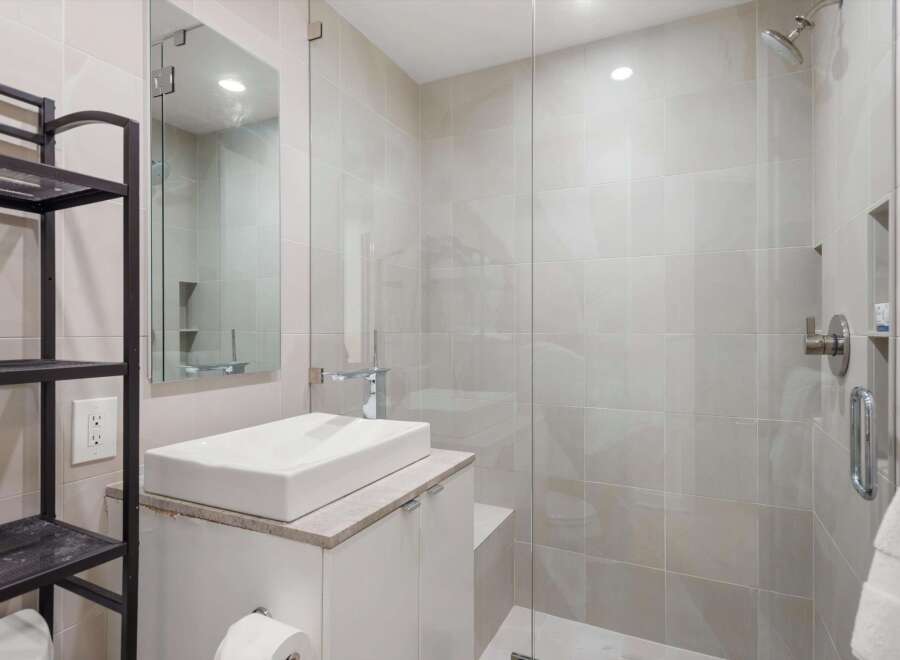 Experience modern luxury in this stunning bathroom featuring a sleek vessel sink atop a white vanity, complemented by a spacious glass-enclosed shower with elegant tilework.
