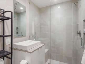 Experience modern luxury in this stunning bathroom featuring a sleek vessel sink atop a white vanity, complemented by a spacious glass-enclosed shower with elegant tilework.