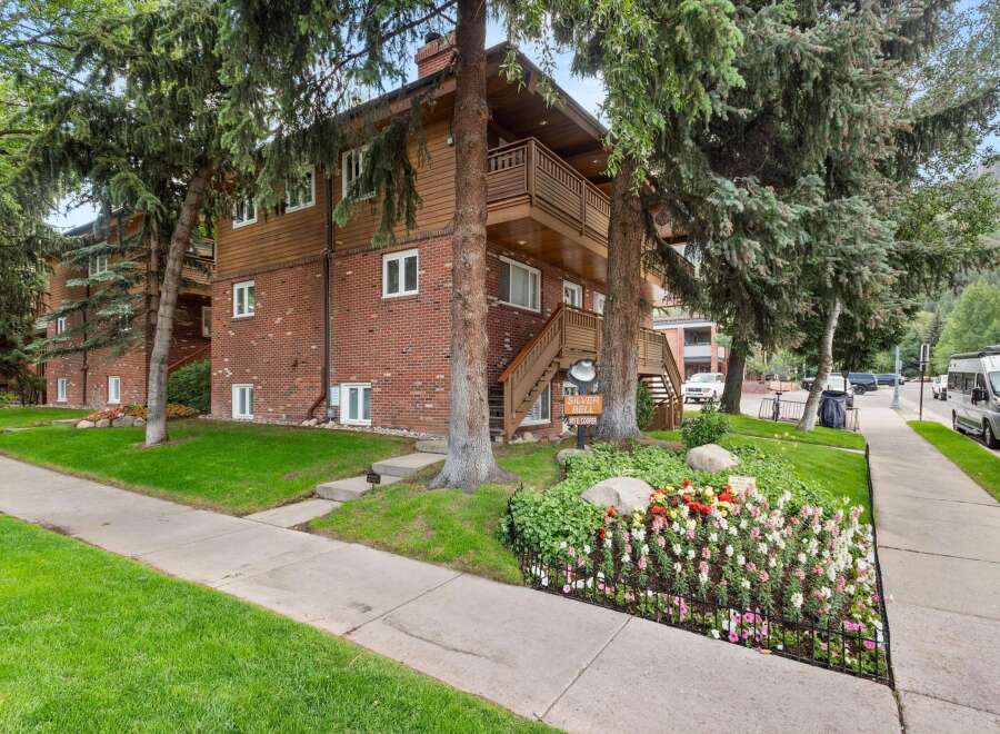 Charming brick and wood-sided apartment building nestled amongst mature trees.