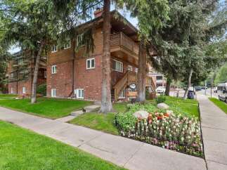Charming brick and wood-sided apartment building nestled amongst mature trees.