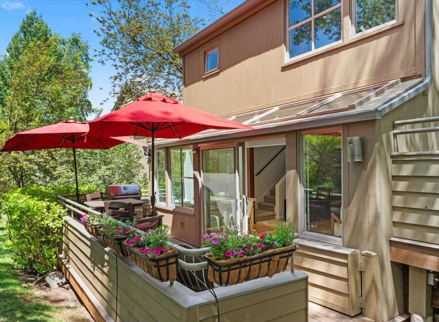 Enjoy outdoor living with this charming patio featuring two red umbrellas, a grill, and ample seating.