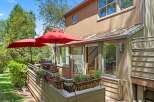 Enjoy outdoor living with this charming patio featuring two red umbrellas, a grill, and ample seating.