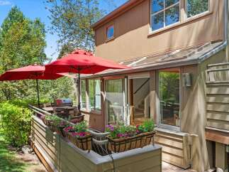 Enjoy outdoor living with this charming patio featuring two red umbrellas, a grill, and ample seating.