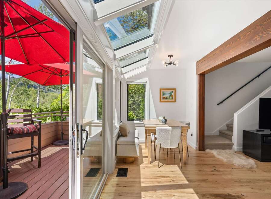Enjoy indoor-outdoor living in this sun-drenched sunroom featuring a retractable glass roof and access to a private deck with red umbrellas.