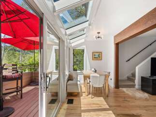 Enjoy indoor-outdoor living in this sun-drenched sunroom featuring a retractable glass roof and access to a private deck with red umbrellas.