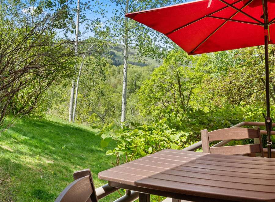 Enjoy the serene mountain views from this charming outdoor dining area, complete with a table, chairs, and a vibrant red umbrella.