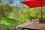 Enjoy the serene mountain views from this charming outdoor dining area, complete with a table, chairs, and a vibrant red umbrella.