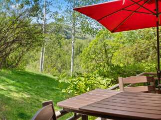 Enjoy the serene mountain views from this charming outdoor dining area, complete with a table, chairs, and a vibrant red umbrella.