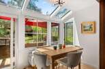 Enjoy abundant natural light in this charming dining area, featuring a stunning skylight and large windows that offer picturesque views of the surrounding greenery.