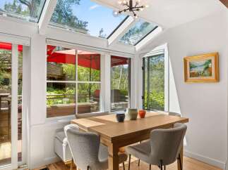 Enjoy abundant natural light in this charming dining area, featuring a stunning skylight and large windows that offer picturesque views of the surrounding greenery.