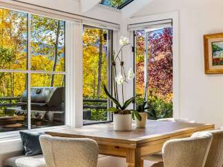 Enjoy breathtaking autumn views from this dining area, featuring large windows that showcase vibrant fall foliage and distant mountains.