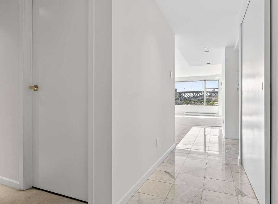 Step into this elegant hallway featuring a striking marble tile floor that leads to a bright living space with large windows offering scenic views.