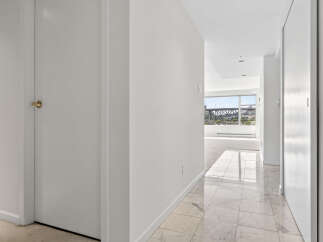 Step into this elegant hallway featuring a striking marble tile floor that leads to a bright living space with large windows offering scenic views.